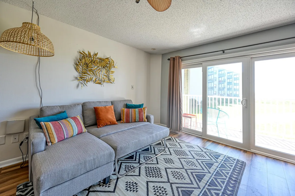 A cozy living room with a comfortable sofa, decorative wall art, and a window that offers a glimpse of the outdoors. The space is softly lit, inviting relaxation, conversation, or taking in sunrise views from inside.