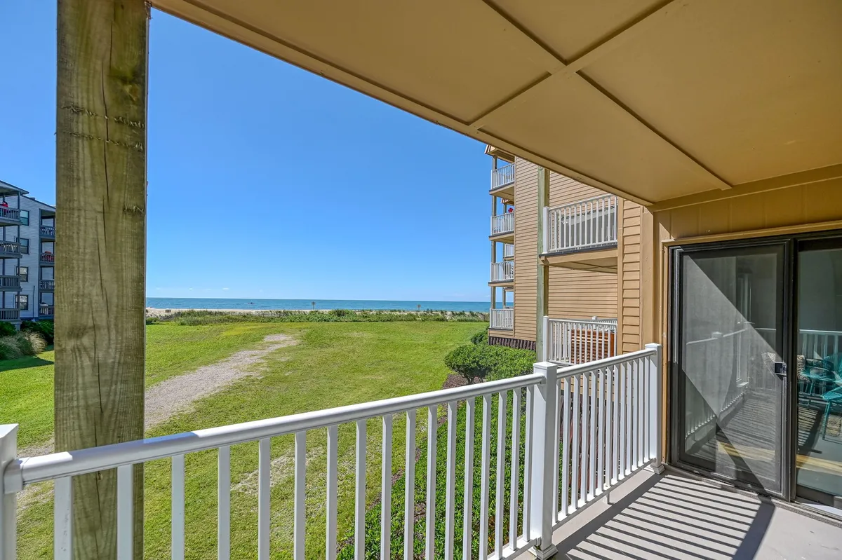 This image captures the stunning ocean view from the balcony, featuring a balcony railing, lush green lawn below, and the vast expanse of the sea beyond. The perspective suggests a peaceful spot to relax and enjoy the ocean breeze, with the potential for sunrise or sunset enjoyment.