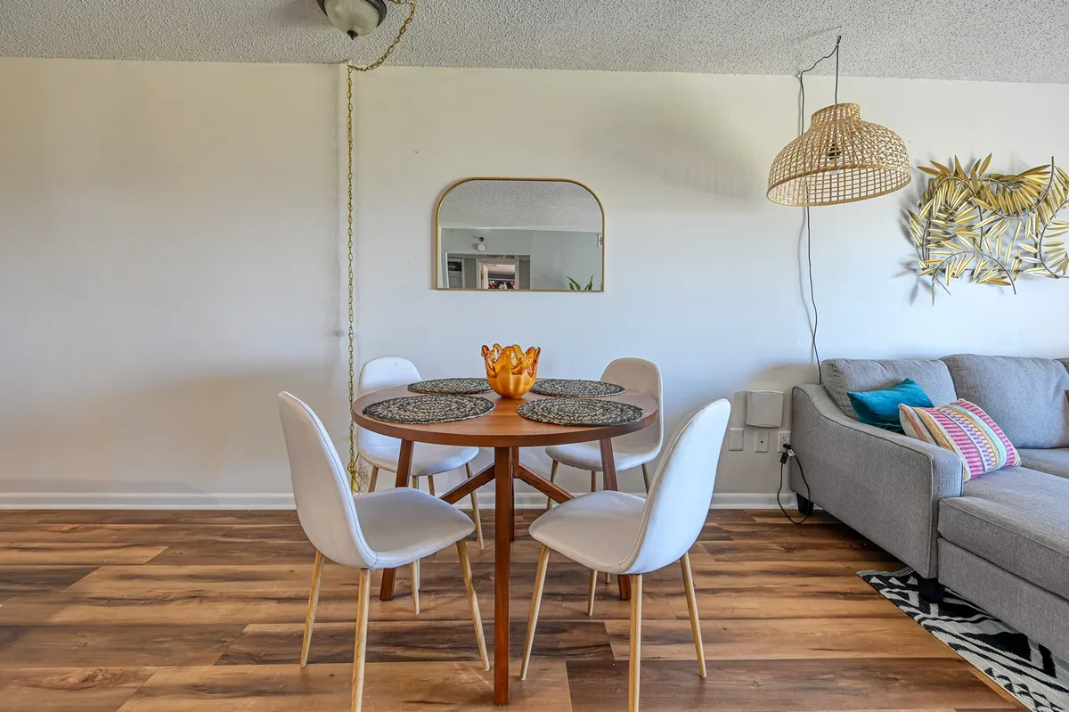A bright, inviting dining area with a table set for casual meals, a decorative bowl as a centerpiece, a woven pendant light overhead, and a comfortable sofa nearby. The scene hints at casual gatherings, shared meals, and relaxed social moments.