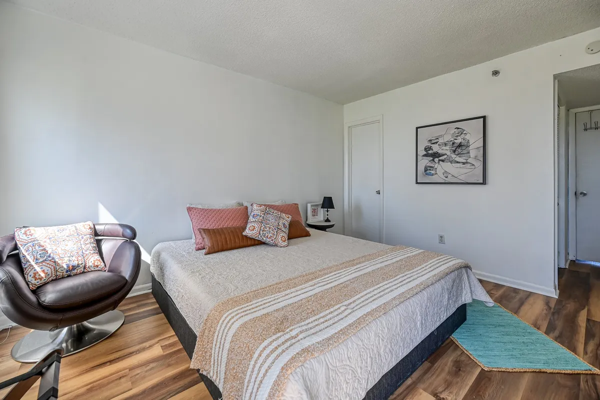A tranquil bedroom with a stylish bed adorned with decorative pillows, a cozy armchair, and calming wall art, offering an inviting haven for rest and relaxation.